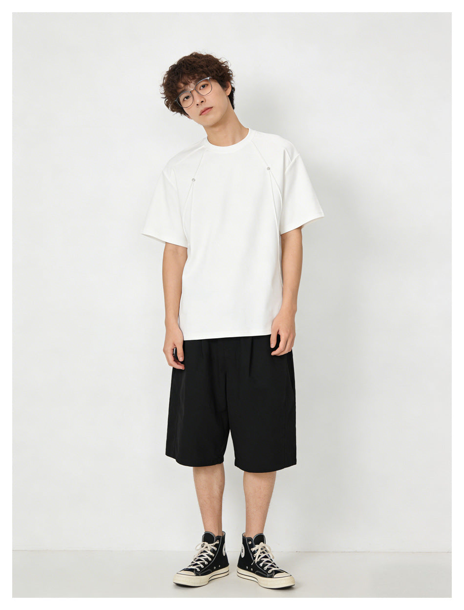 Model wearing a white short-sleeve crew-neck shirt with shoulder seams and black knee-length shorts.