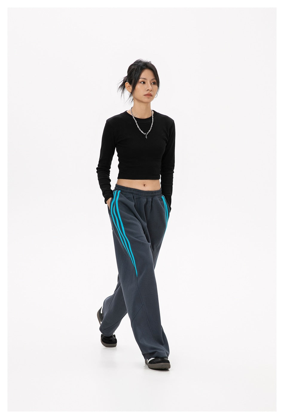 Model wearing charcoal wide-leg track pants with bright turquoise side stripes and a black cropped long-sleeve top.