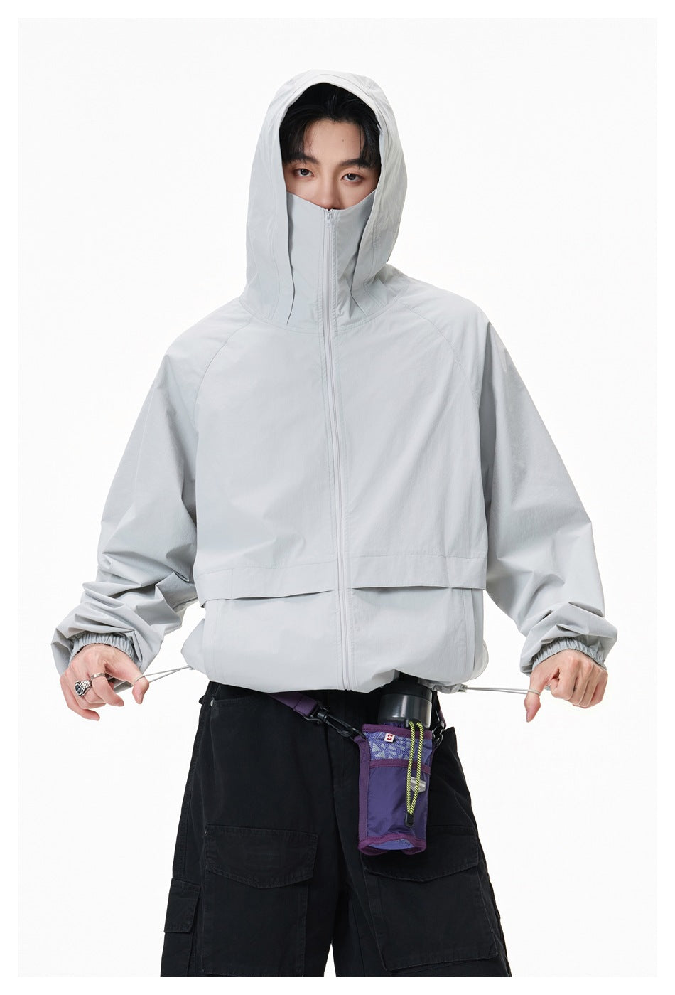 Model wearing a light gray hooded zip jacket with a high face-covering collar and black cargo pants.