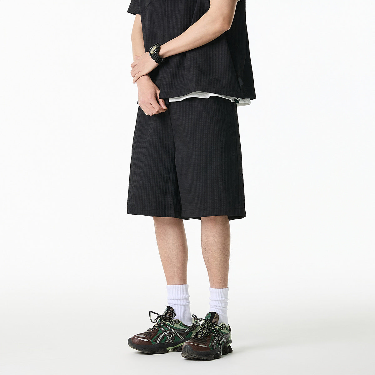 Cropped front view of a model wearing a black textured short-sleeve shirt and matching knee-length shorts.
