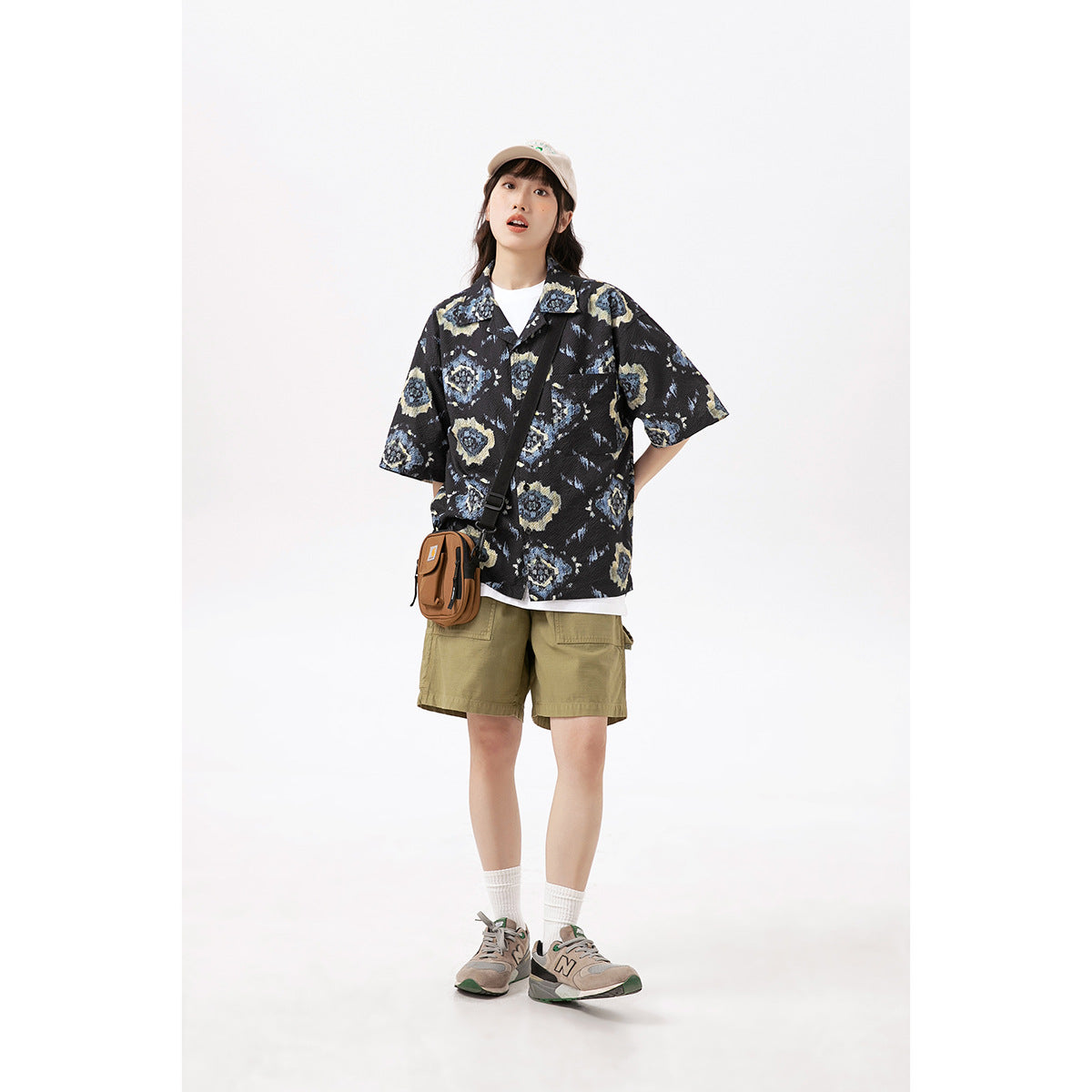 Model wearing a black short-sleeve shirt with blue and cream motifs and olive cargo shorts.