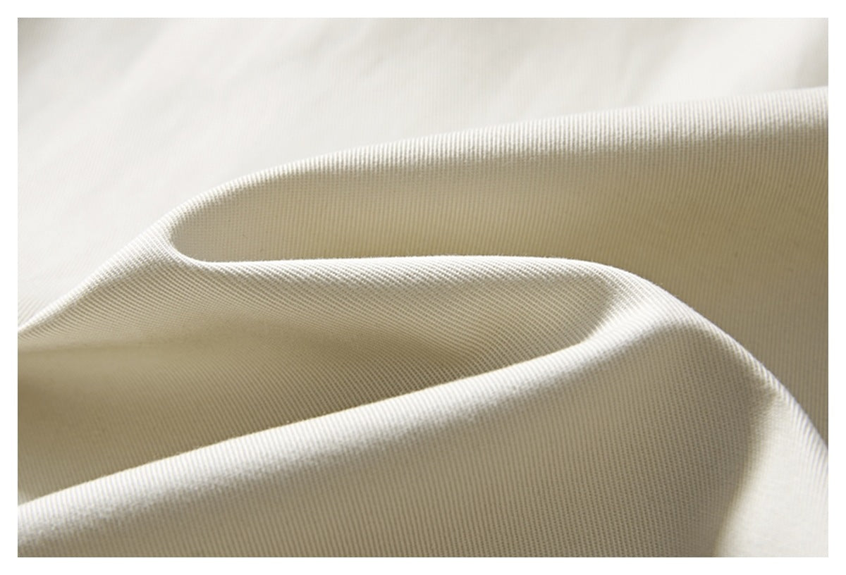 Macro view of the fine diagonal weave and drape of cream trouser fabric.