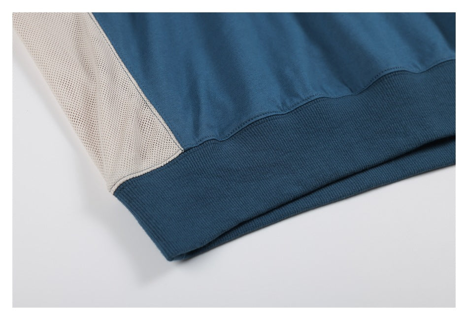 Close-up of a blue sweatshirt hem with a cream mesh side panel and ribbed waistband.