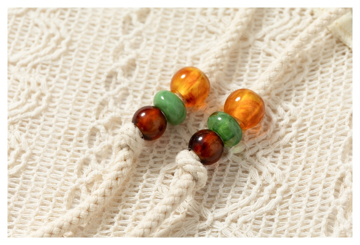 Close-up of amber, green, and brown round buttons on braided cords against a cream open-knit garment.