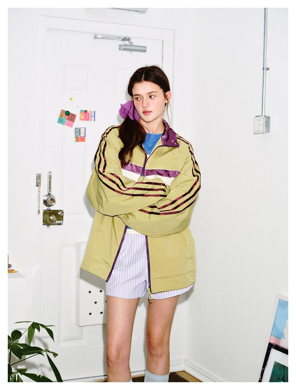 Model wearing an olive track jacket with purple and cream panels and burgundy sleeve stripes.