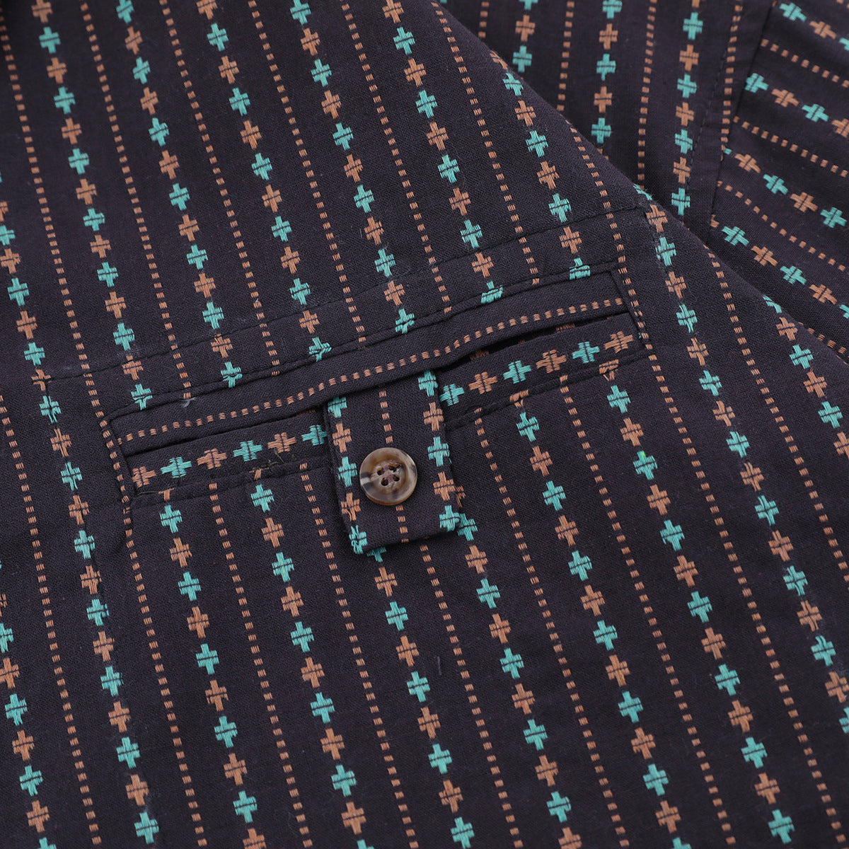 Close-up of a dark patterned shirt showing its buttoned cuff, pocket edge, turquoise and rust motifs, and dotted stripes.