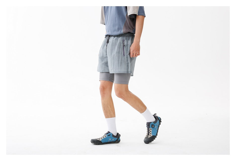 Angled front view of a person wearing pale blue-gray running shorts with zip pockets over gray compression shorts.