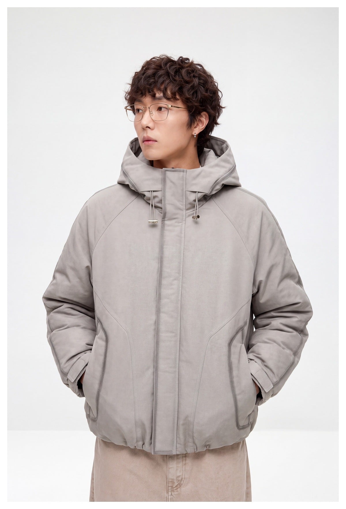 Model wearing a light gray hooded jacket zipped closed, shown from the front with hands in pockets.