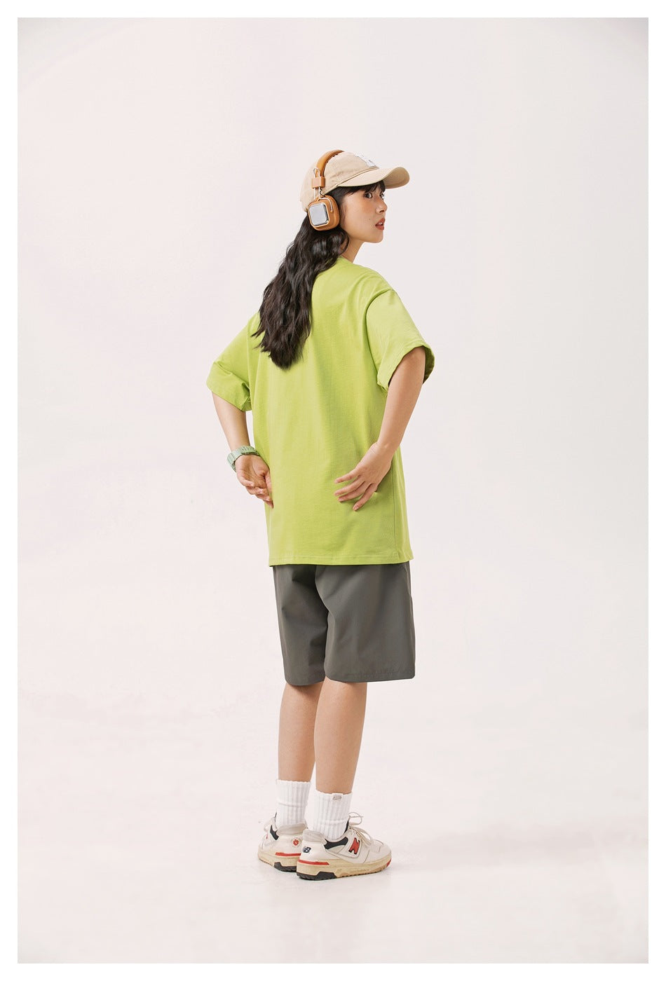 Rear three-quarter view of a model wearing a plain-back lime green oversized T-shirt and gray shorts.