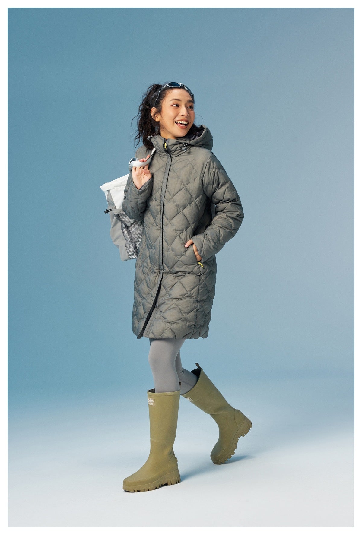 Model wearing a gray diamond-quilted hooded coat, shown walking in olive knee-high boots.