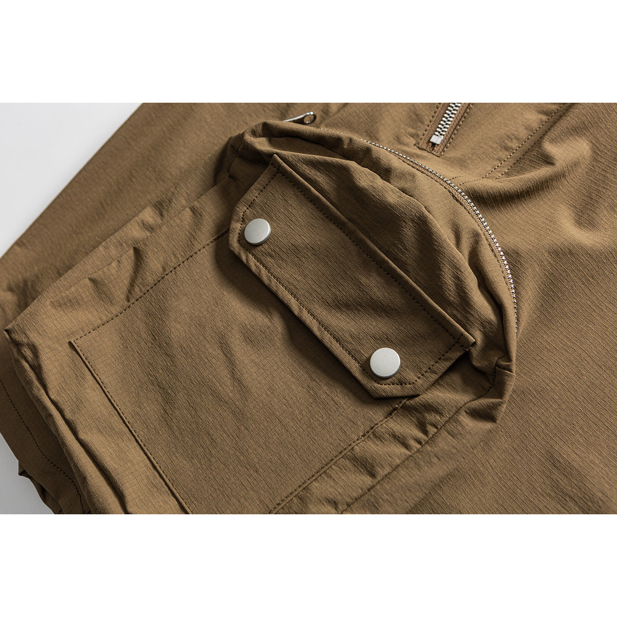 Close-up of brown shorts with a flap cargo pocket secured by two snaps and a curved zipper nearby.