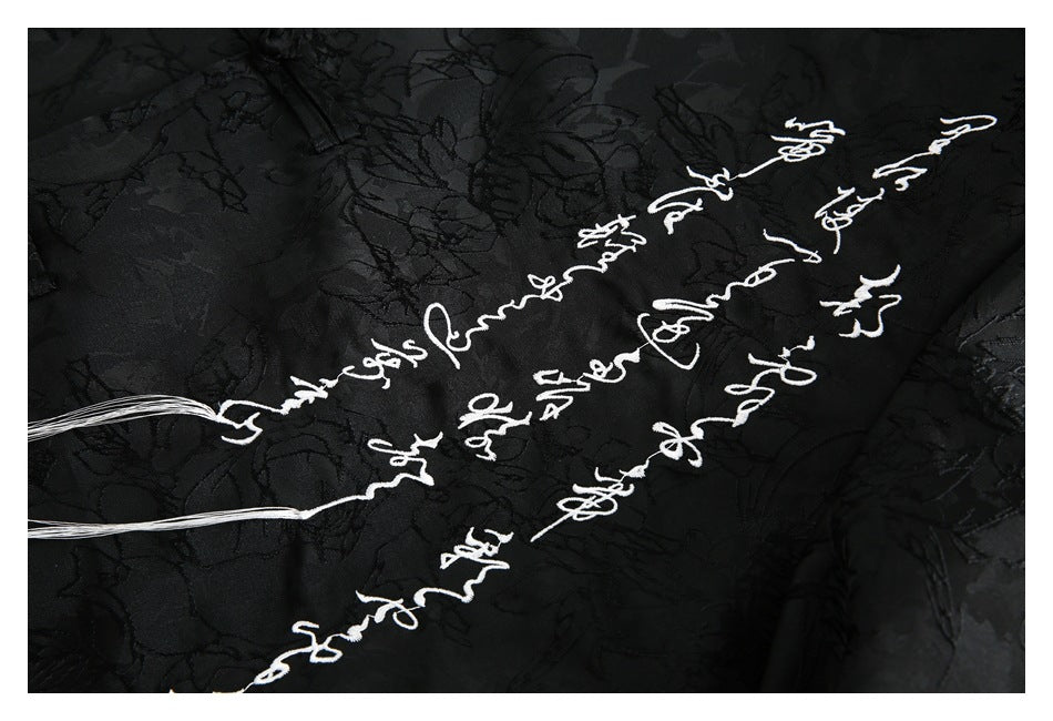 Close-up of white cursive embroidery on black floral-patterned fabric.