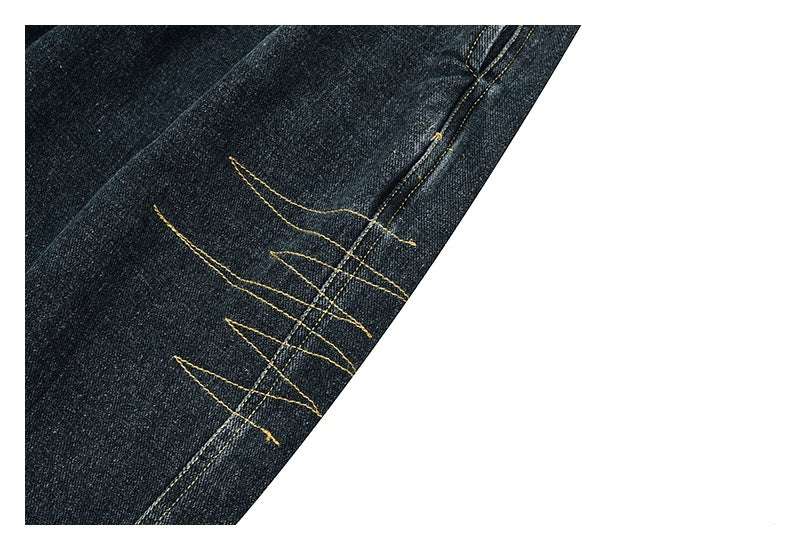 Cropped close-up of angular golden-yellow stitching beside a seam on dark denim.