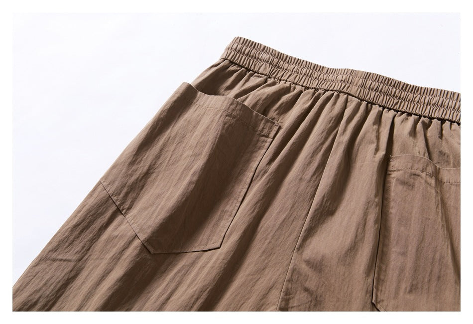 Close-up of taupe trousers showing the gathered elastic waistband and large patch pockets.