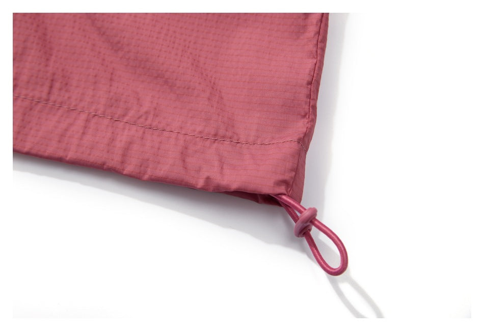 Close-up of a dusty rose garment hem with a stitched seam and looped drawcord.