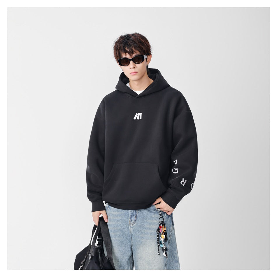 Model wearing a black oversized hoodie with a white chest emblem and sleeve lettering, paired with light-wash jeans.