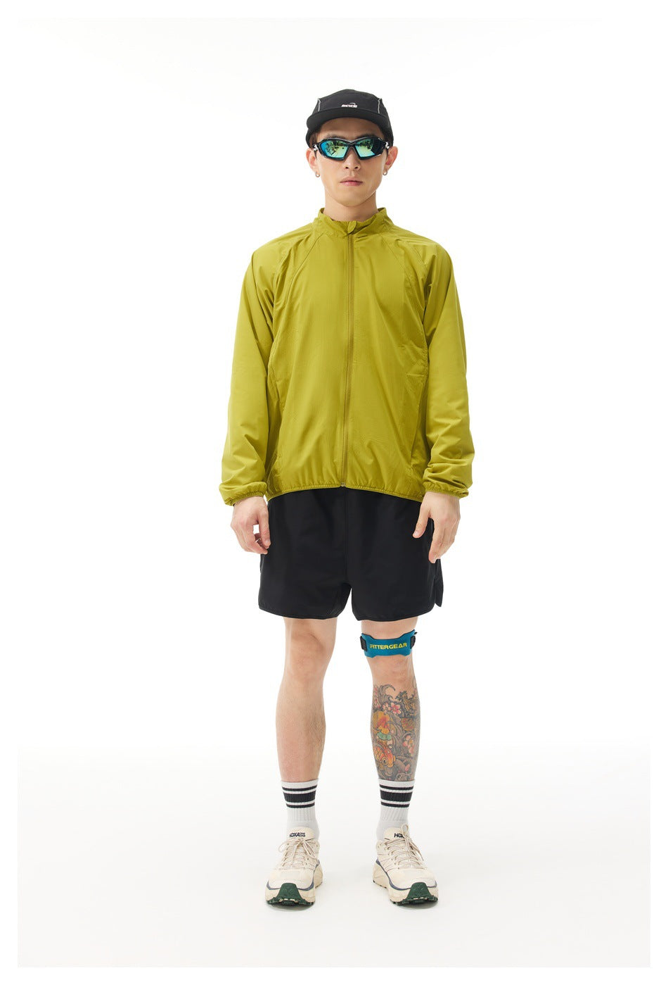 Man wearing a yellow-green zip-up stand-collar jacket with black shorts, front view