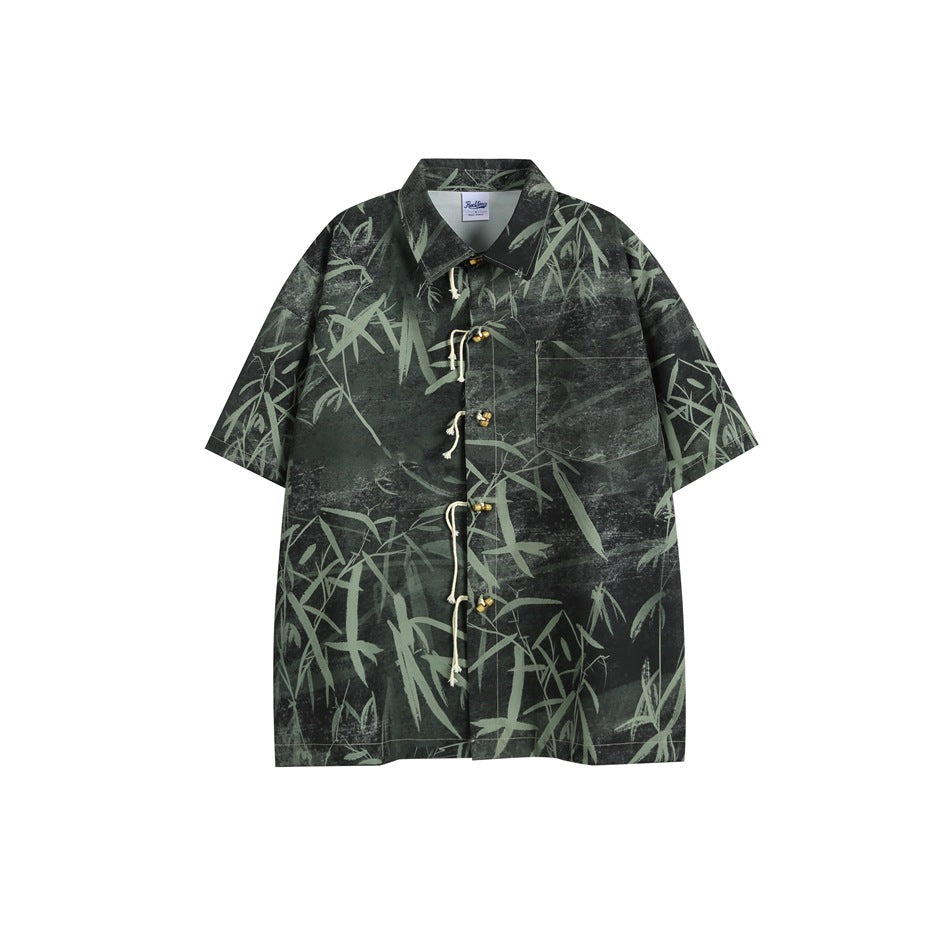 Flat-lay front of a dark green-black short-sleeve shirt with a sage bamboo print, rope-loop toggle closure and chest pocket