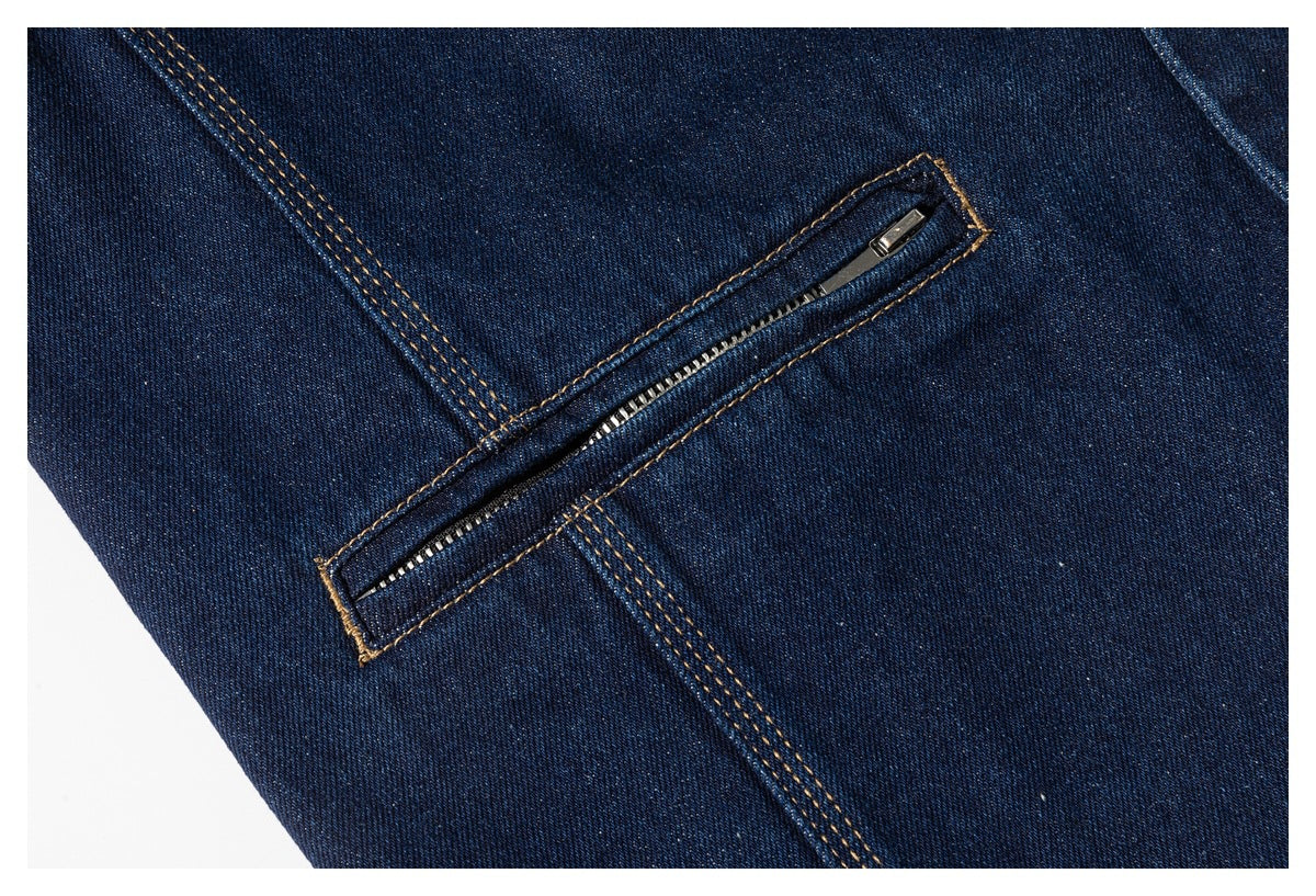 Close-up of a diagonal zippered pocket on dark blue denim with golden stitching.