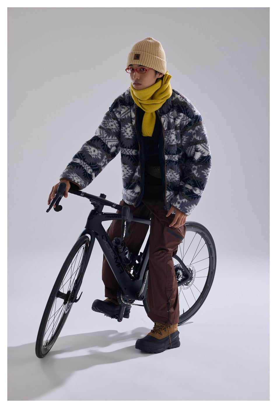 Model wearing a gray patterned fleece jacket and brown cargo pants while standing over a road bicycle.