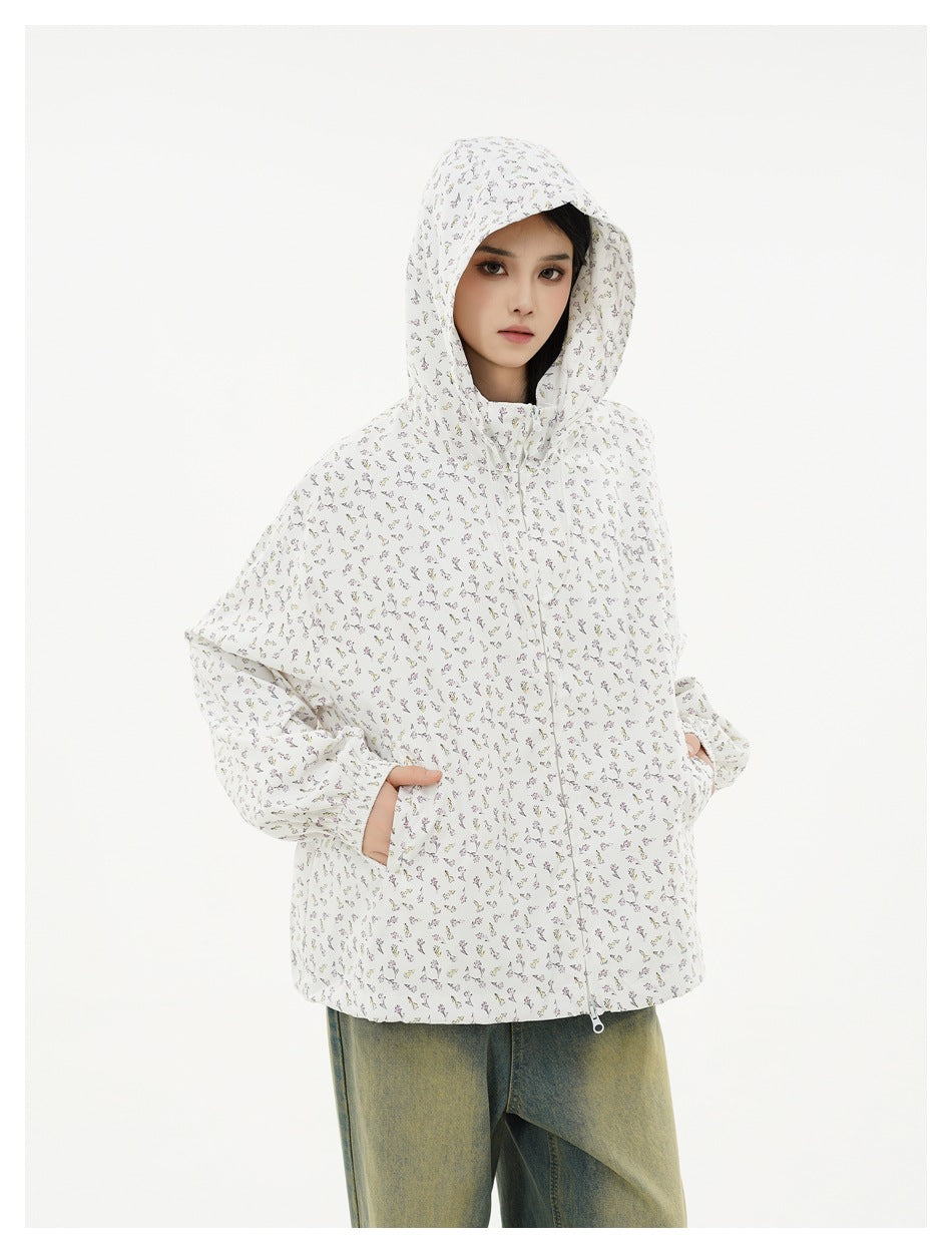Model wearing a white hooded zip jacket with a small multicolor floral print and loose sleeves.