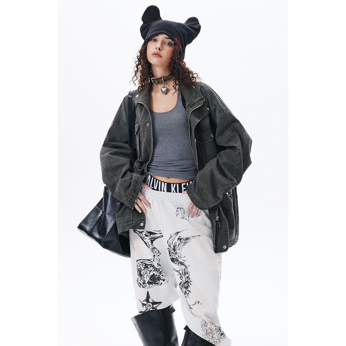 Model wearing an oversized charcoal jacket, gray tank, printed white pants, and black ear-shaped beanie.