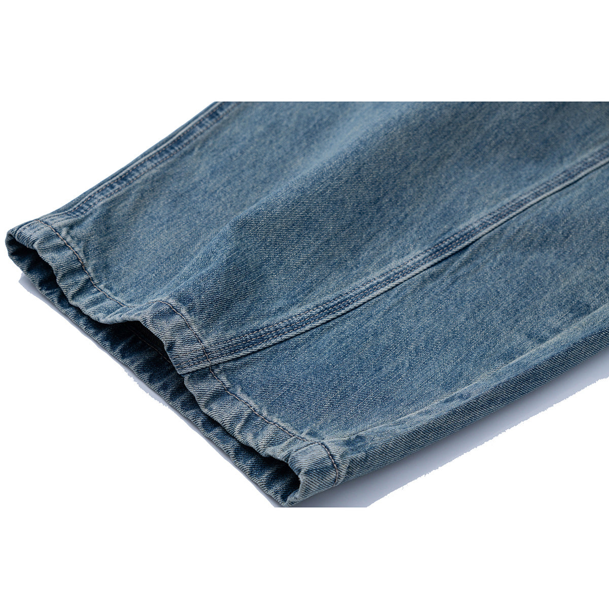 Close-up of the stitched hem and leg seam of faded blue jeans.