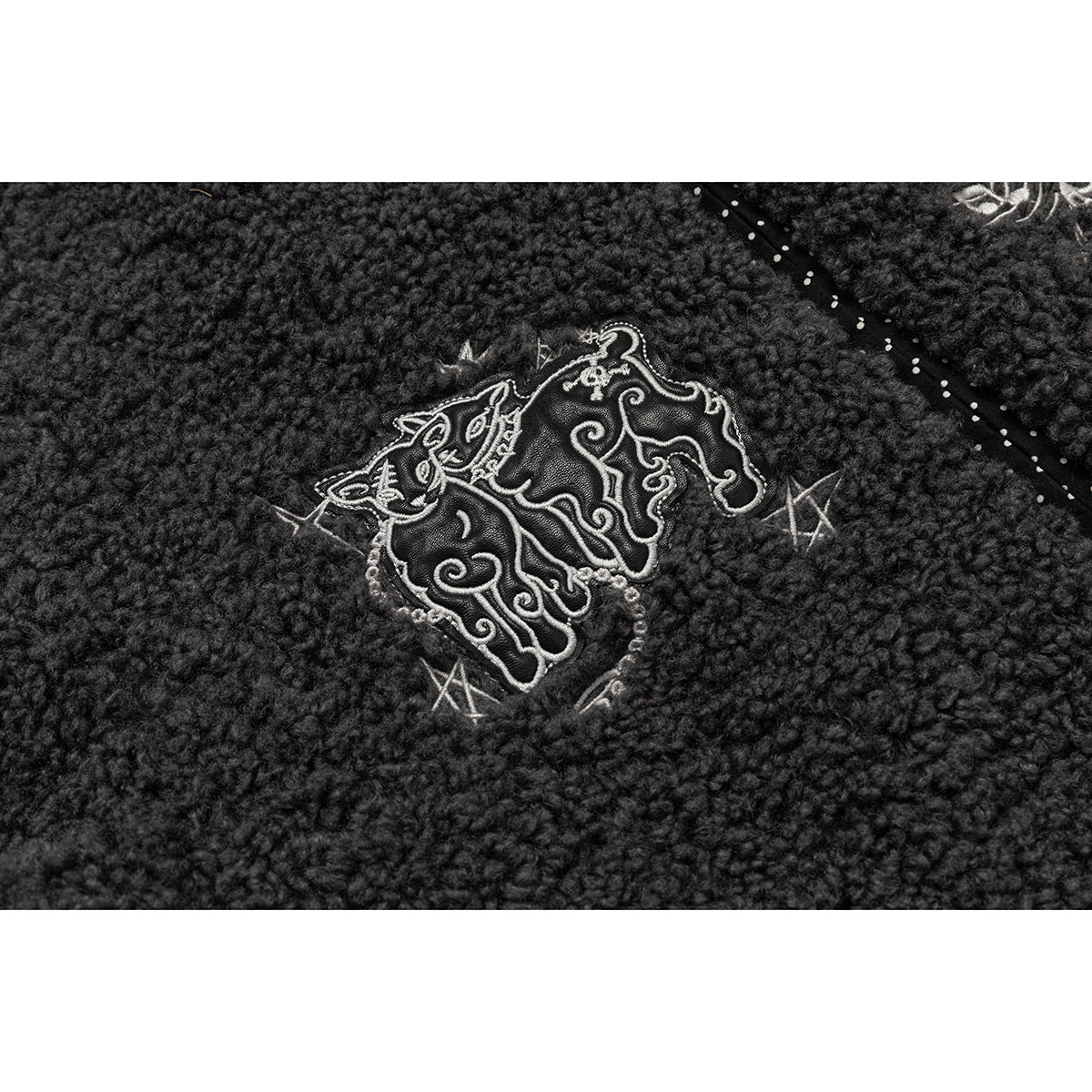 Close-up of an ornate light-colored embroidered motif on charcoal nubby fabric.