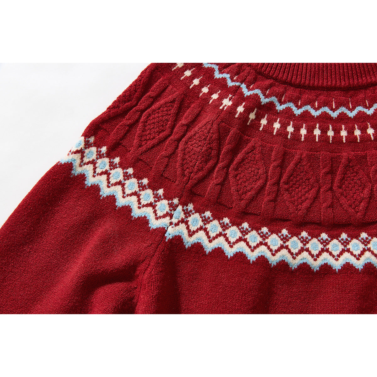 Close-up of a red sweater sleeve and body with raised cable-knit texture and a blue-and-cream patterned band.