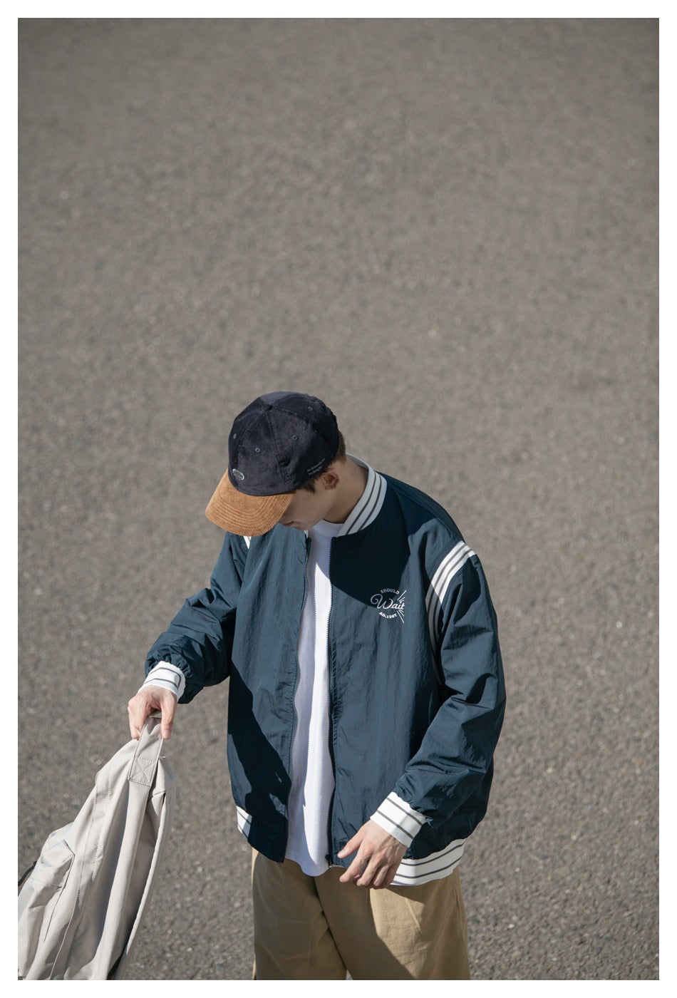 Close view of a model wearing a dark teal jacket with white striped trim and a small scripted chest design.