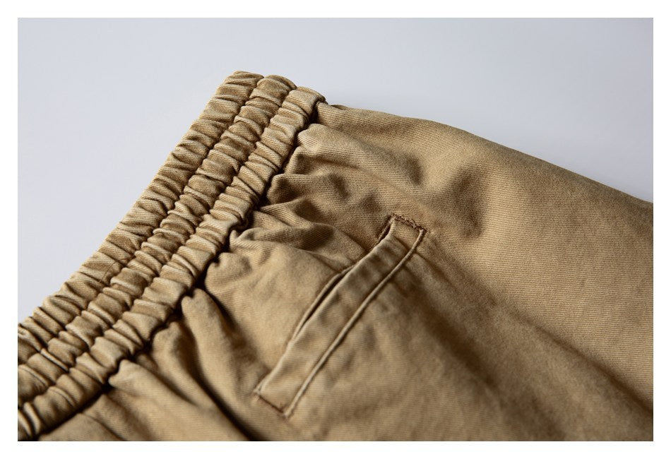 Close-up of tan trousers showing the elastic waistband and slanted pocket stitching.