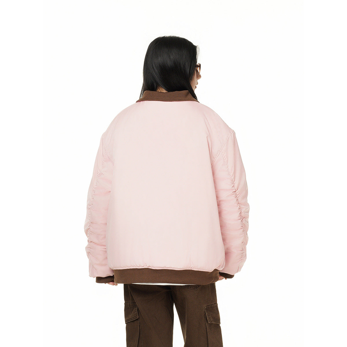 Back view of a model wearing a pale pink jacket with a dark brown collar and hem, paired with brown cargo pants.