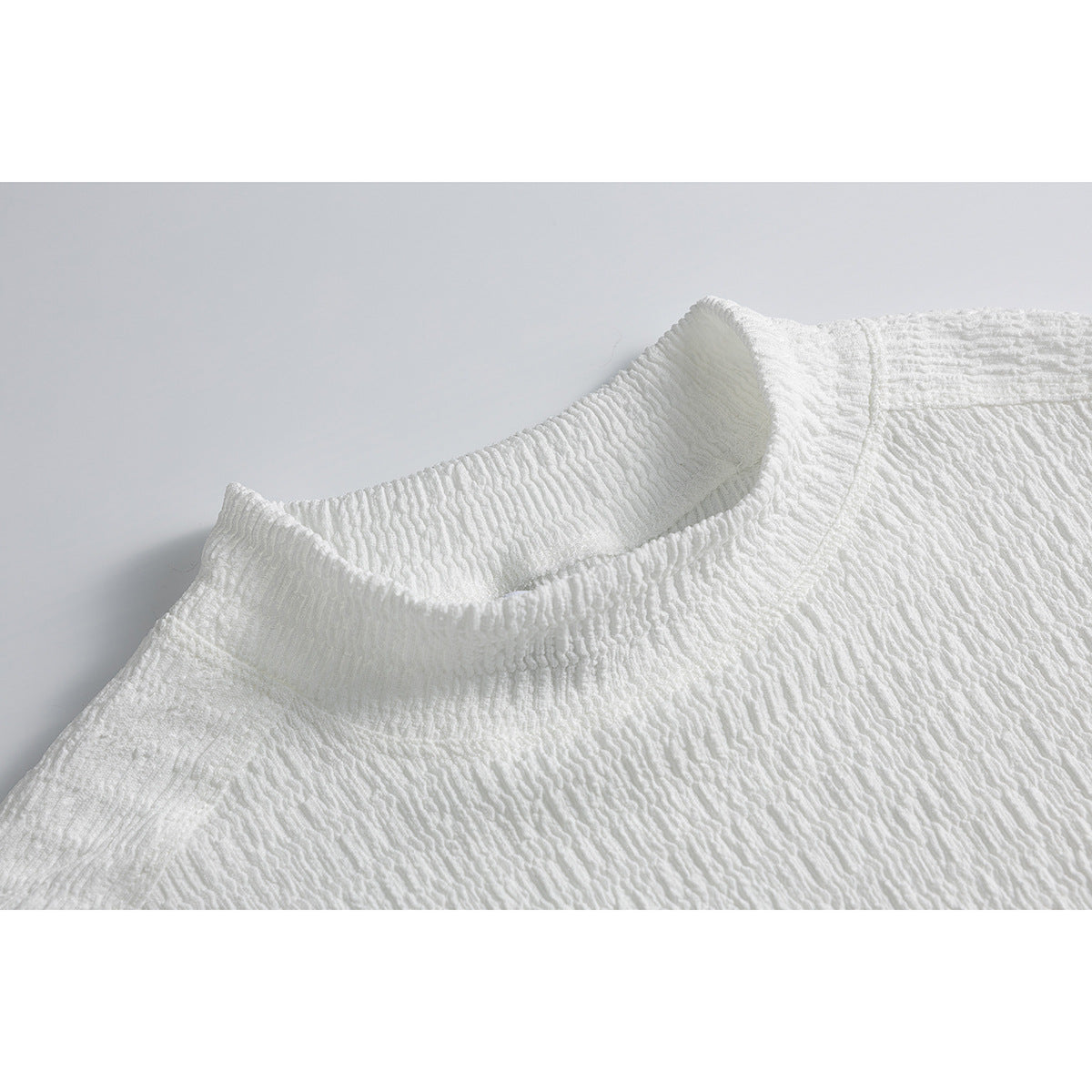Close-up of a white textured shirt showing its raised mock neck and upper shoulder.