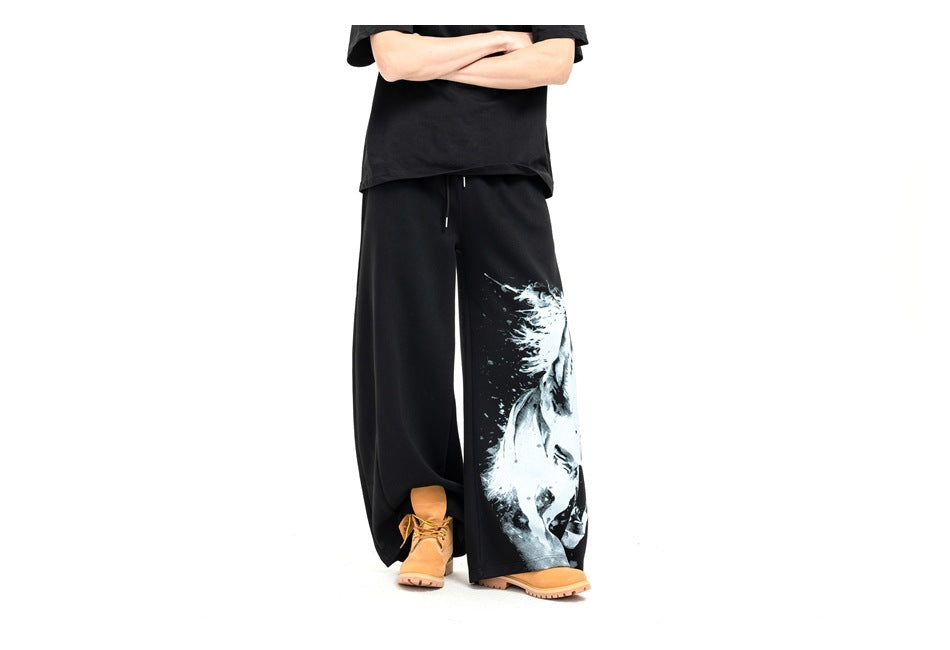 Model wearing black wide-leg pants with a large white horse graphic on one leg, a black shirt and tan boots.