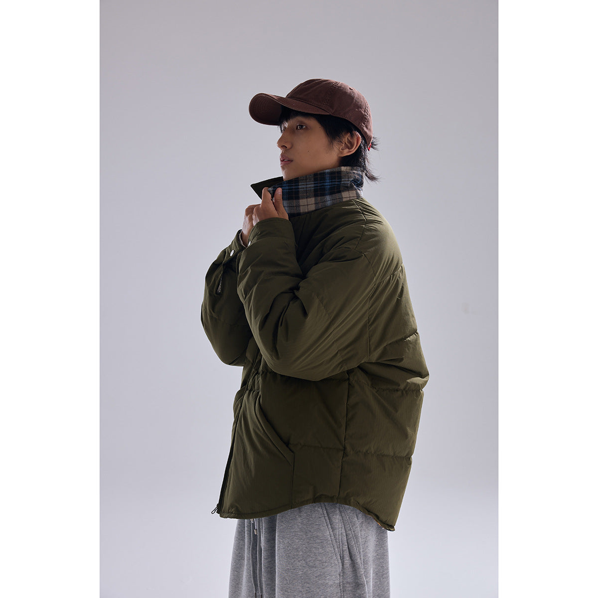 Side view of a model wearing an olive padded jacket with a plaid inner collar and loose gray pants.