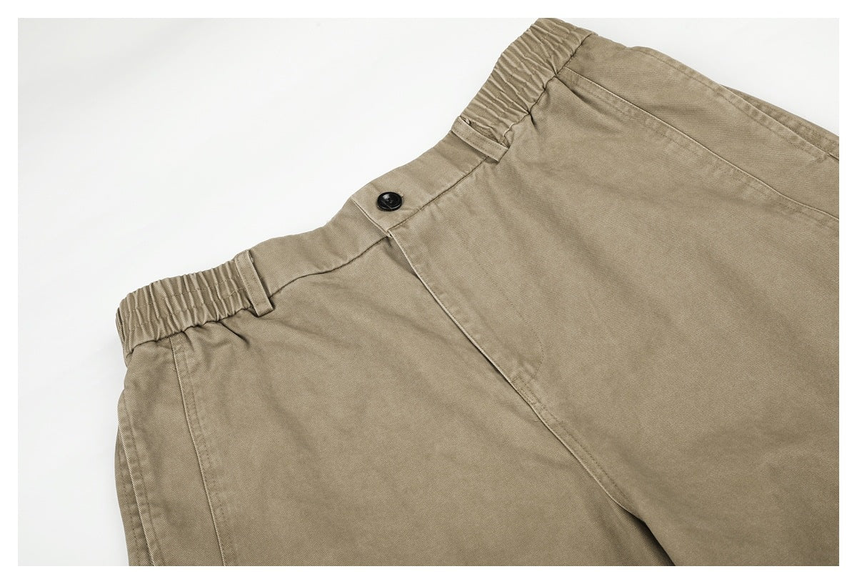 Close-up of beige pants showing the elasticated waistband, belt loops, and black button closure.