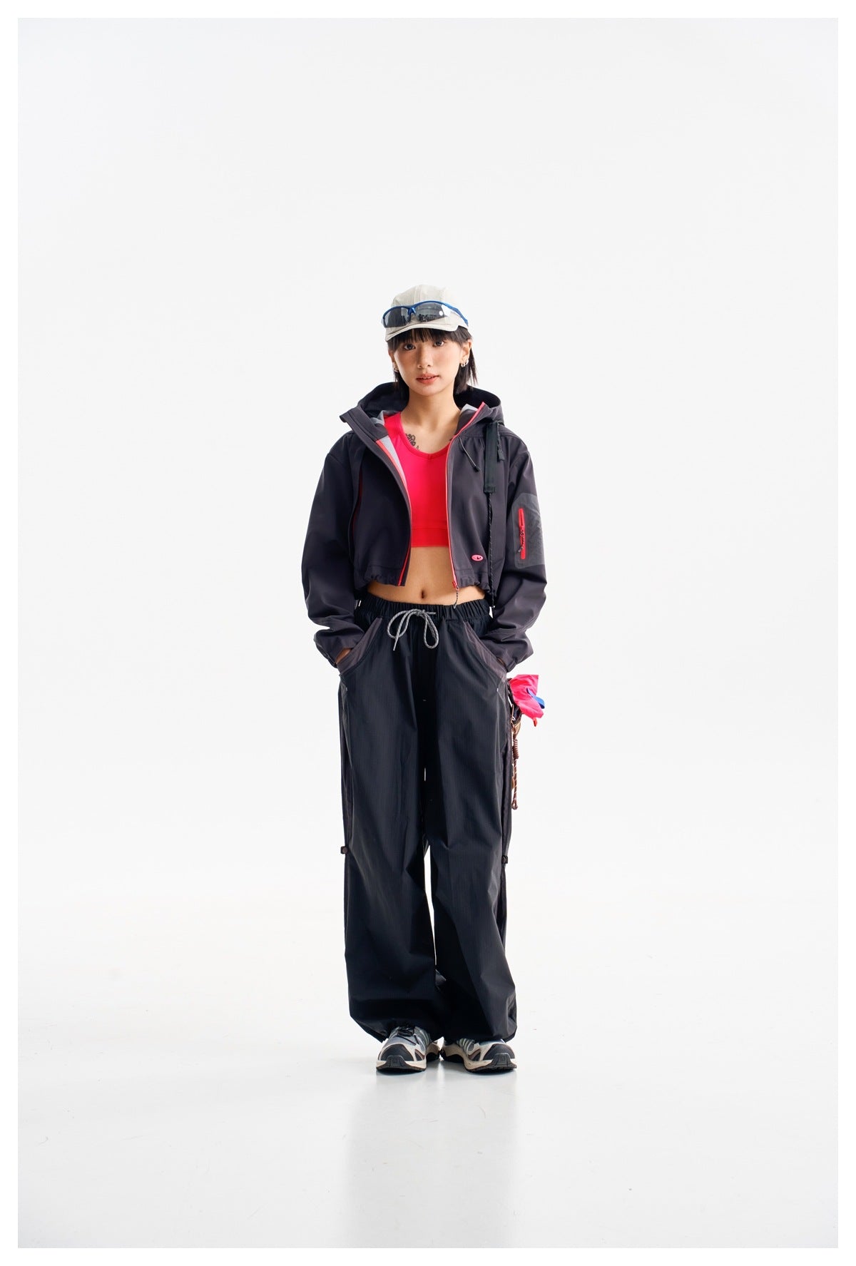 Full-length model wearing a dark cropped jacket with pink trim, a bright pink top, and loose dark pants.