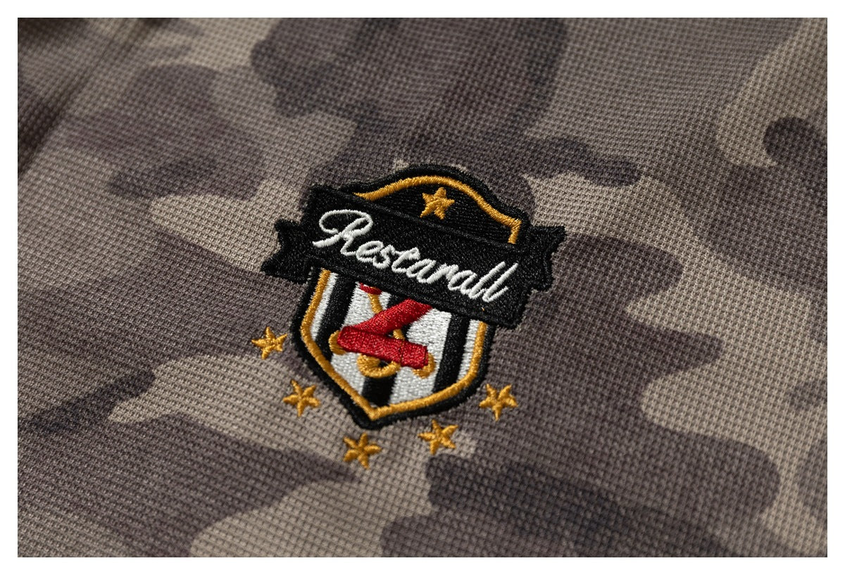 Close-up of an embroidered black, white, red, and gold shield crest on gray-brown camouflage fabric.