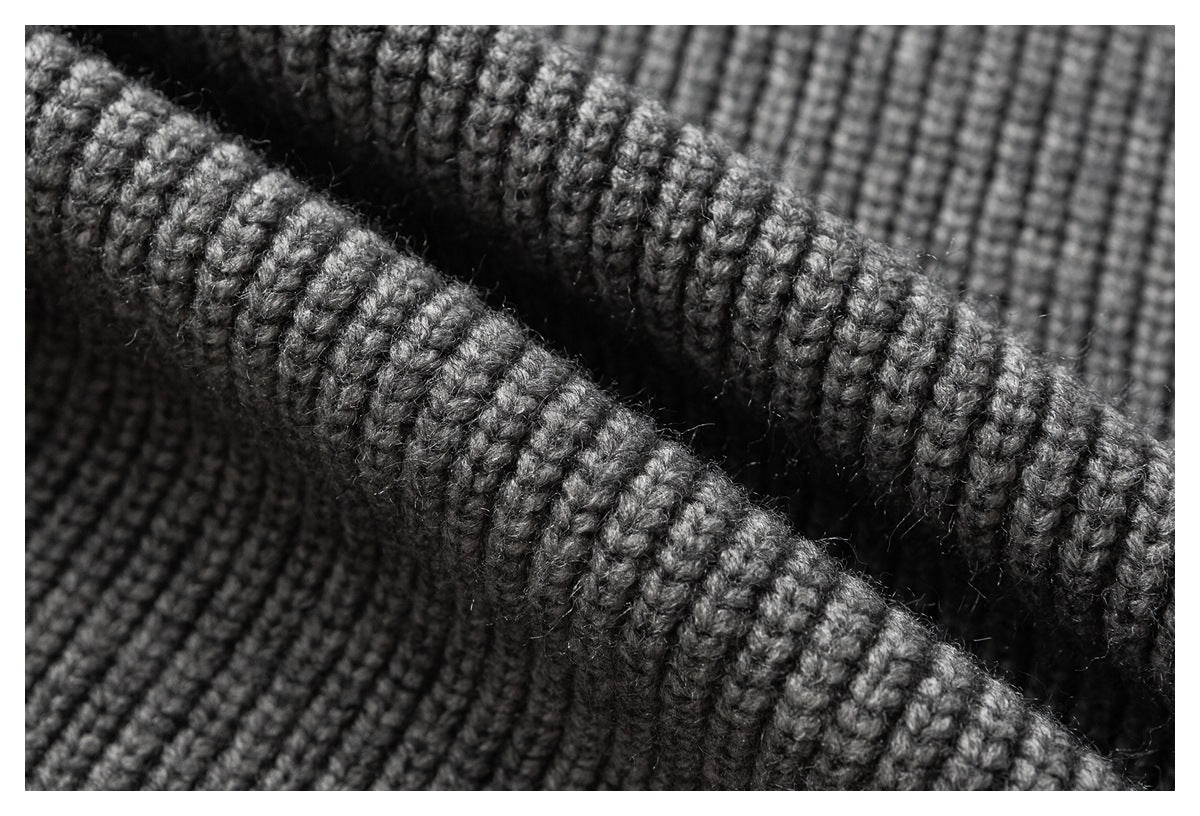 Close-up of dark gray chunky knit fabric with a folded edge and visible looped texture.
