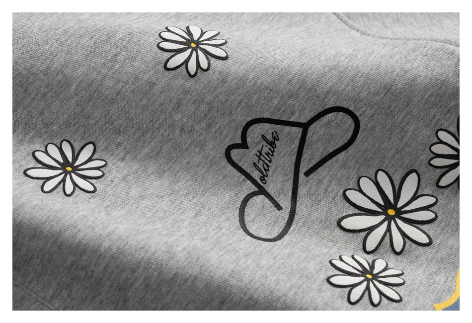 Close-up of black script artwork and several white daisies with yellow centers on gray fabric.