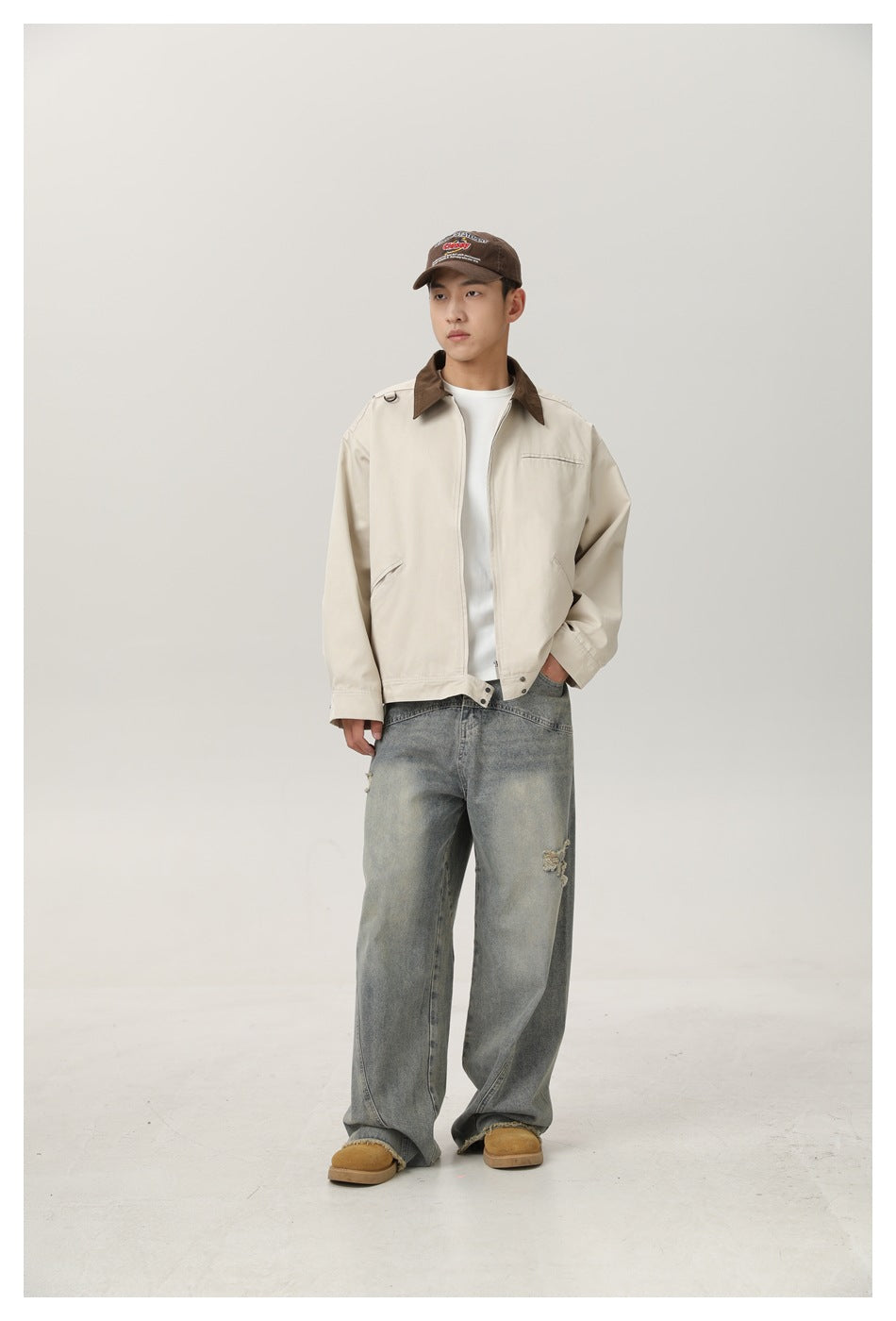 Full-length front view of a model wearing a cream jacket with a brown collar and loose gray jeans.