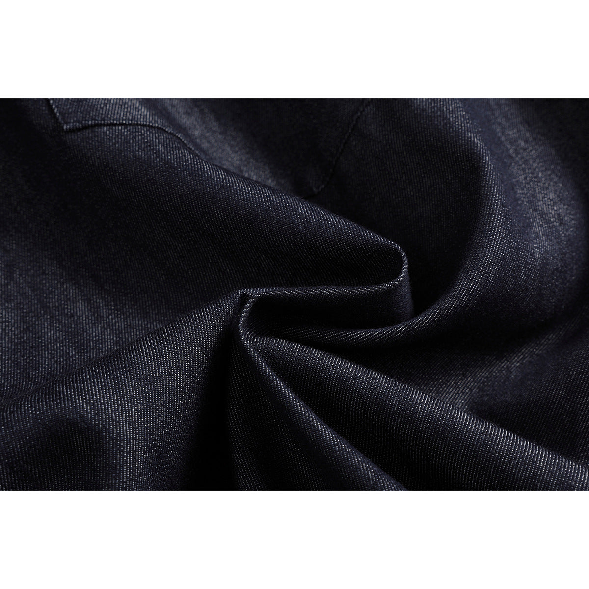 Macro view of dark indigo fabric gathered into folds, showing its fine diagonal weave.