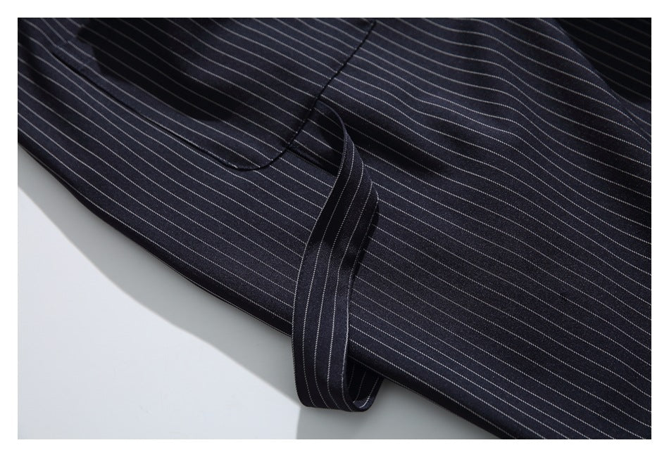 Close-up of dark pinstriped trousers showing a curved pocket seam and a narrow fabric tie.