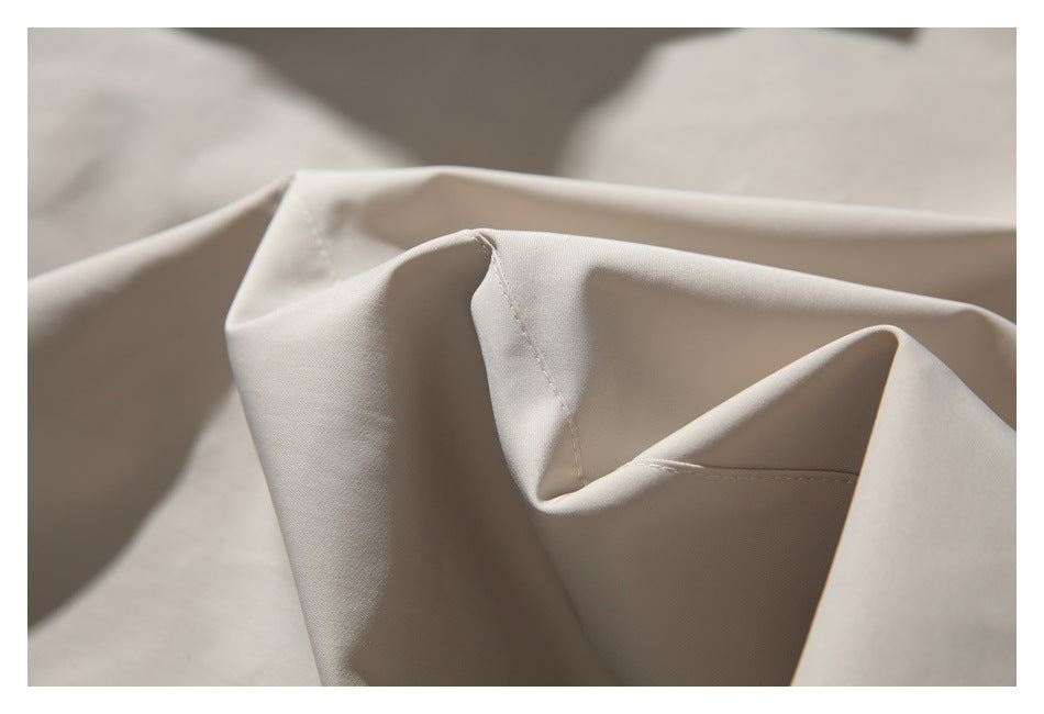Close-up of light beige jacket fabric and stitched seams, showing its smooth surface and folds.