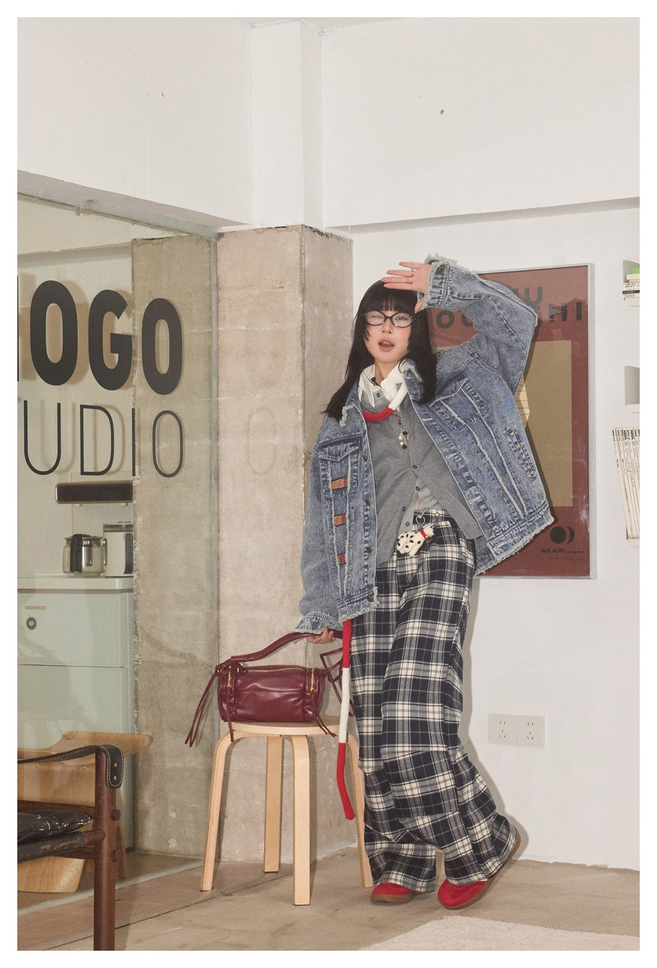 Model wearing the blue frayed denim jacket open over a gray cardigan and plaid wide-leg pants, one arm raised