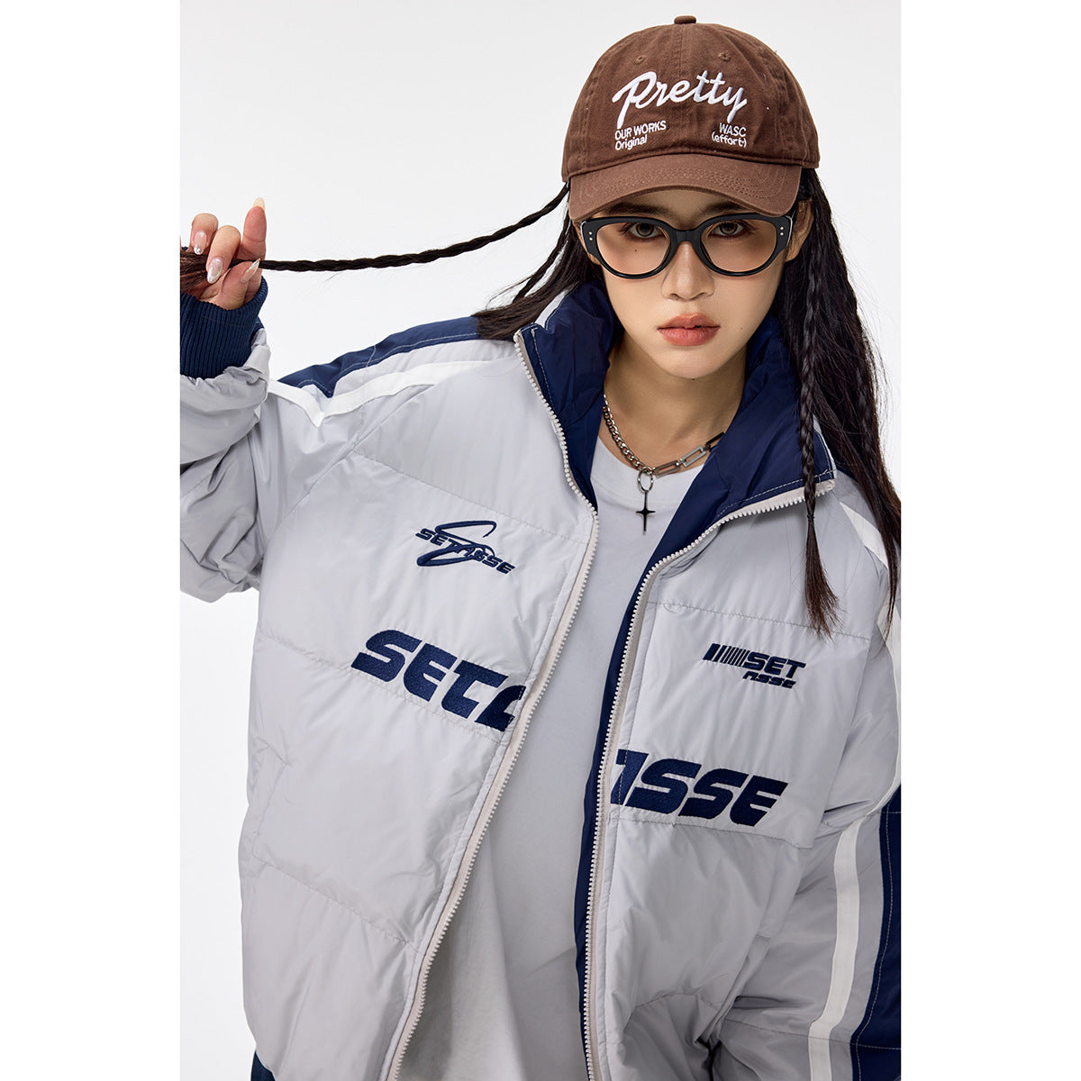 Close view of a model in the light gray and navy padded jacket, showing its collar, zipper, sleeve stripes and chest