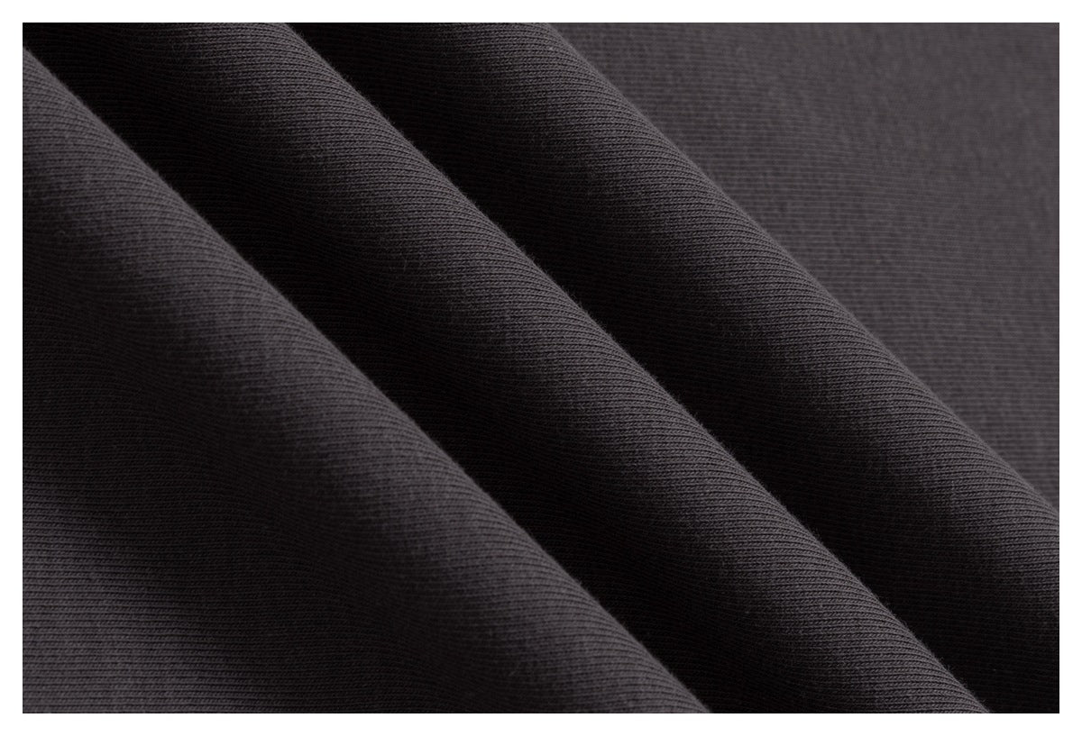 Close-up of dark charcoal fabric folded into diagonal ridges, showing a fine, tightly woven texture.