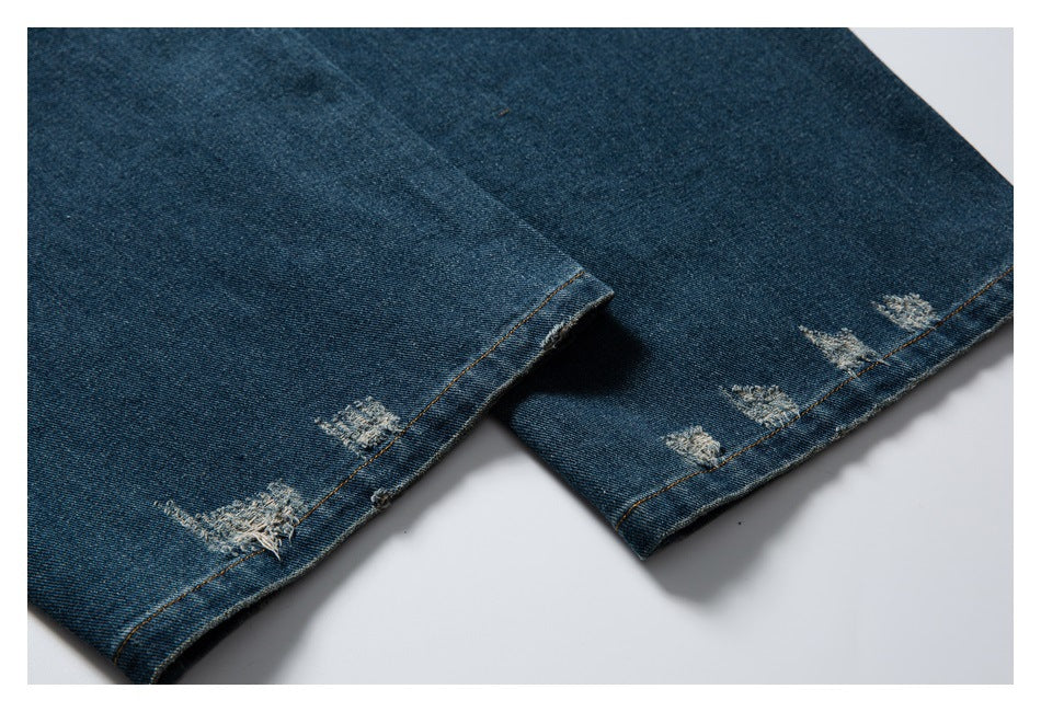 Close-up of dark blue denim leg hems with several distressed patches and contrast stitching.
