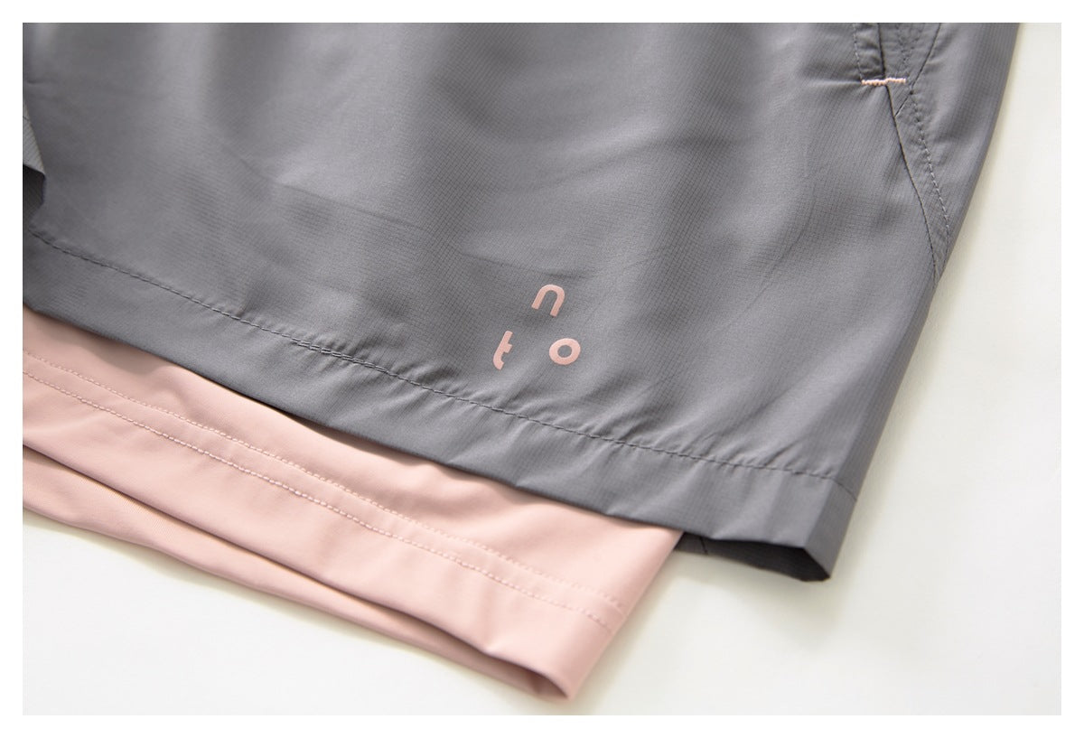 Close-up of gray shorts with a small pink leg print and a pale pink garment layered beneath the hem.