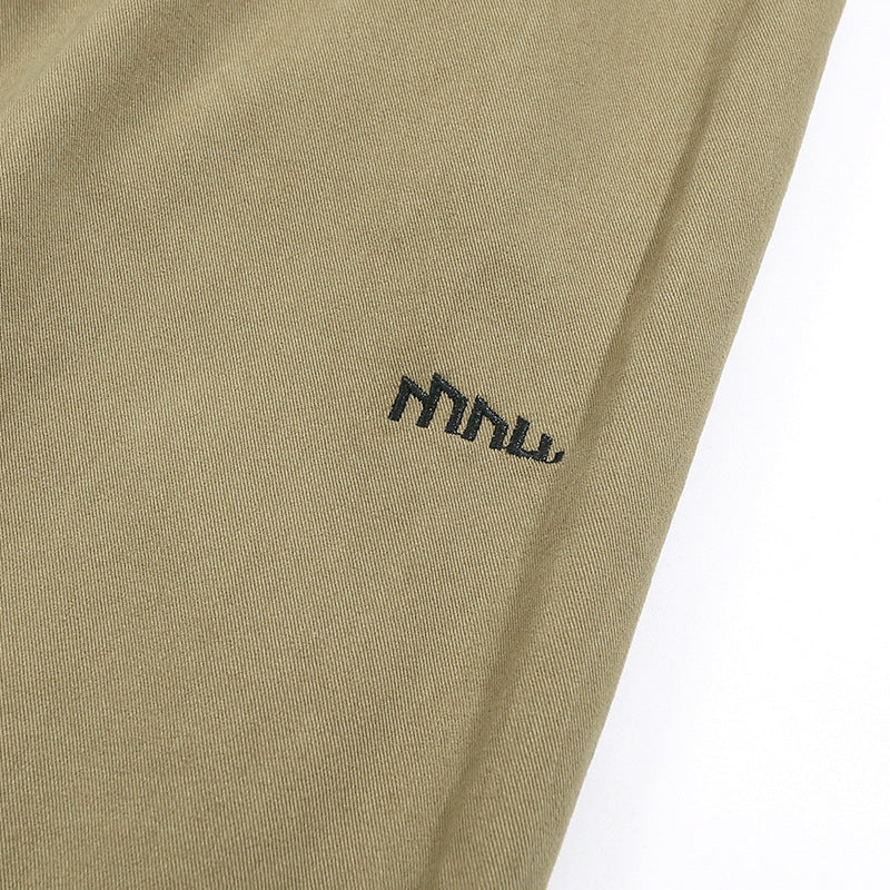Close-up of khaki trouser fabric with a small dark embroidered logo.